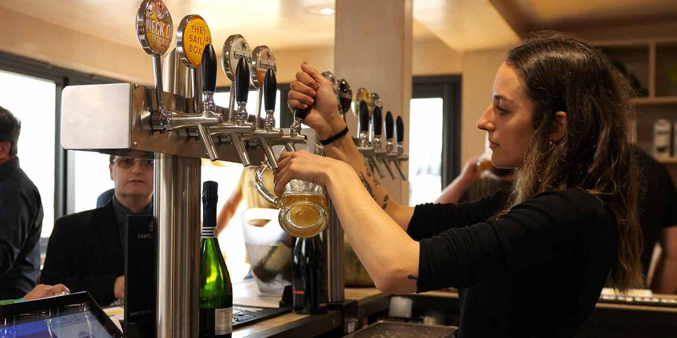 A female bar tender pulling a pint of draught beer to a male customer