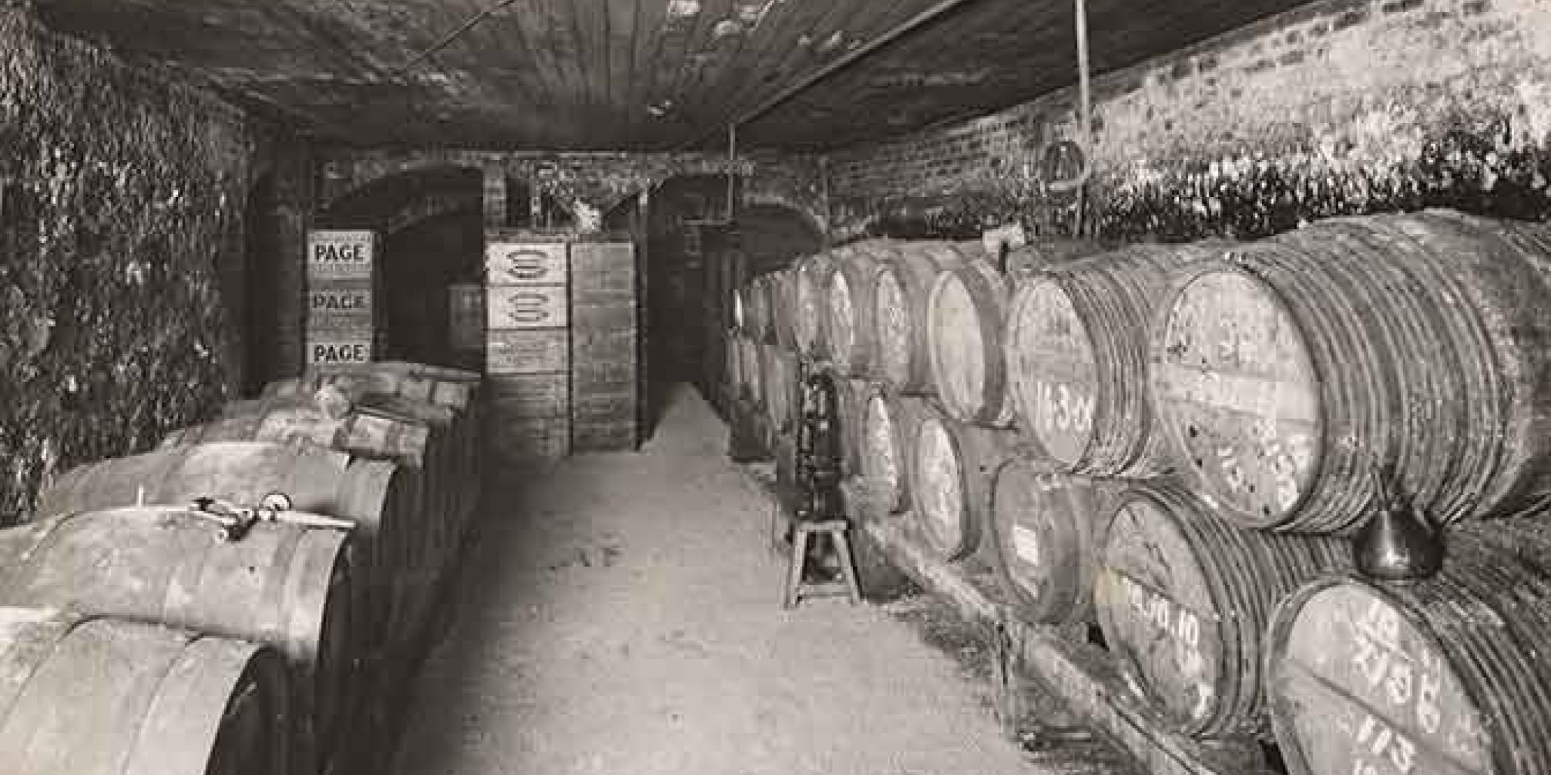 Black and white photo of an old cellar storing boxes of wine and barrels of beer